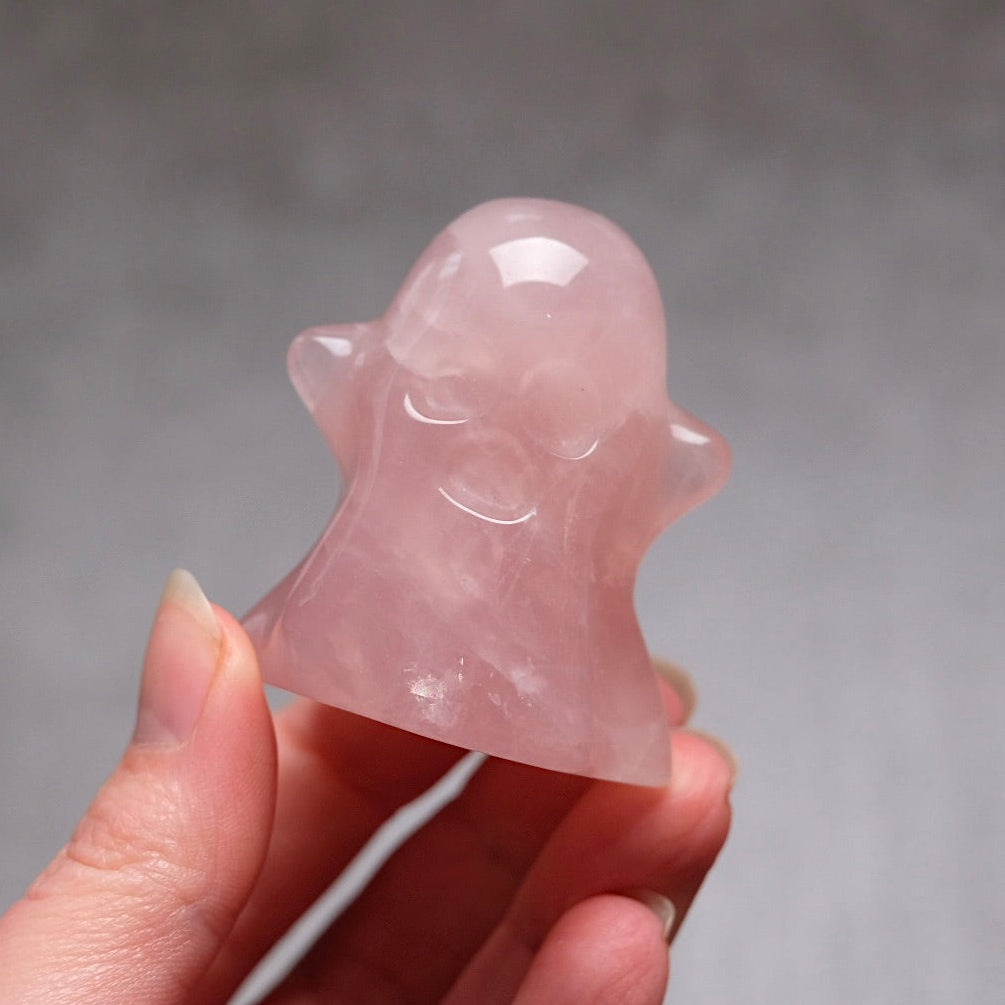 Pink crystal ghost figurine held in a hand against a gray background