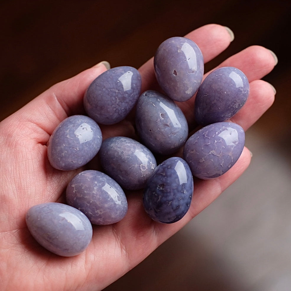 Hand holding purple stones in small egg shapes, against a blurred background