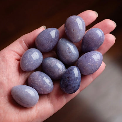 Hand holding purple stones in small egg shapes, against a blurred background
