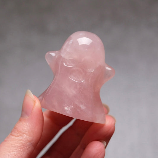 Pink crystal ghost figurine held in a hand against a gray background